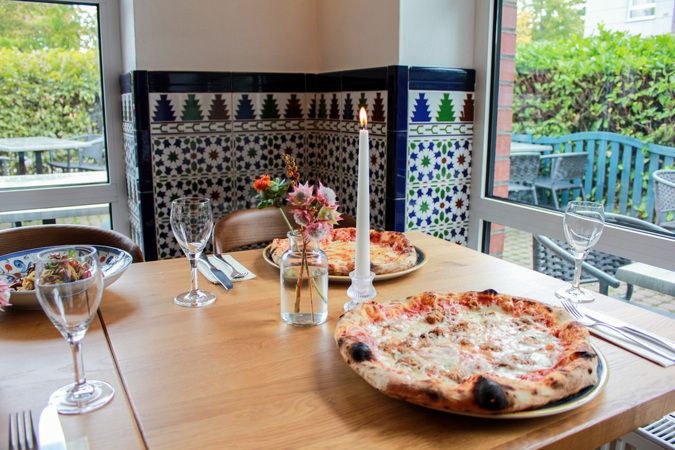 Gedeckter Tisch mit frisch gebackener Pizza im Gastraum der Piazza Italiana
